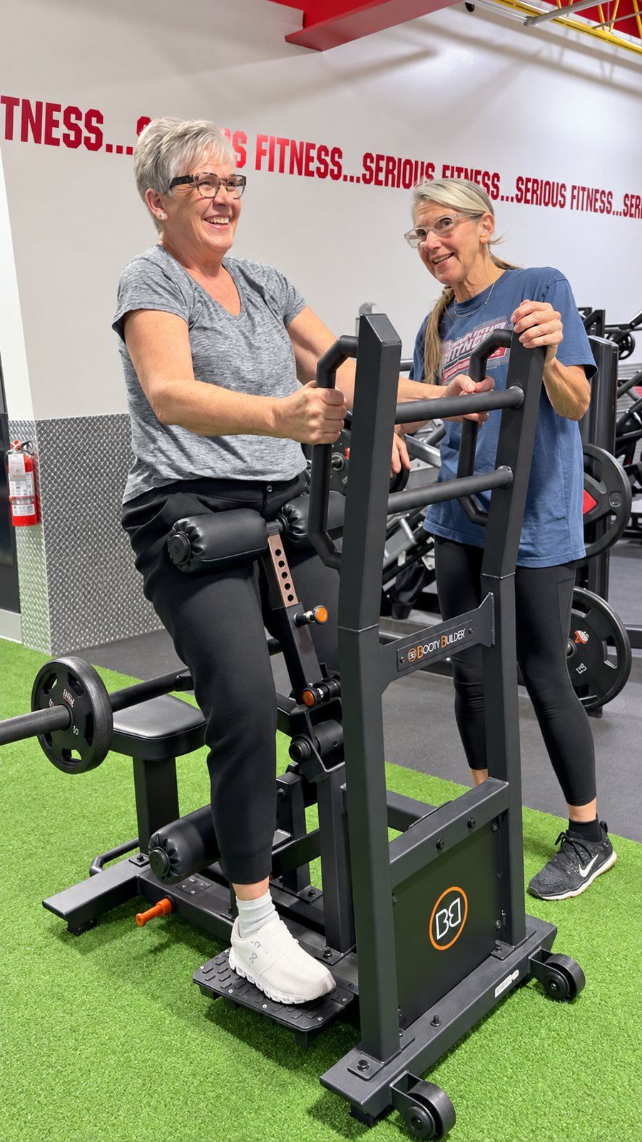 Two friends laughing together on a Booty Builder machine at Super Future Fitness